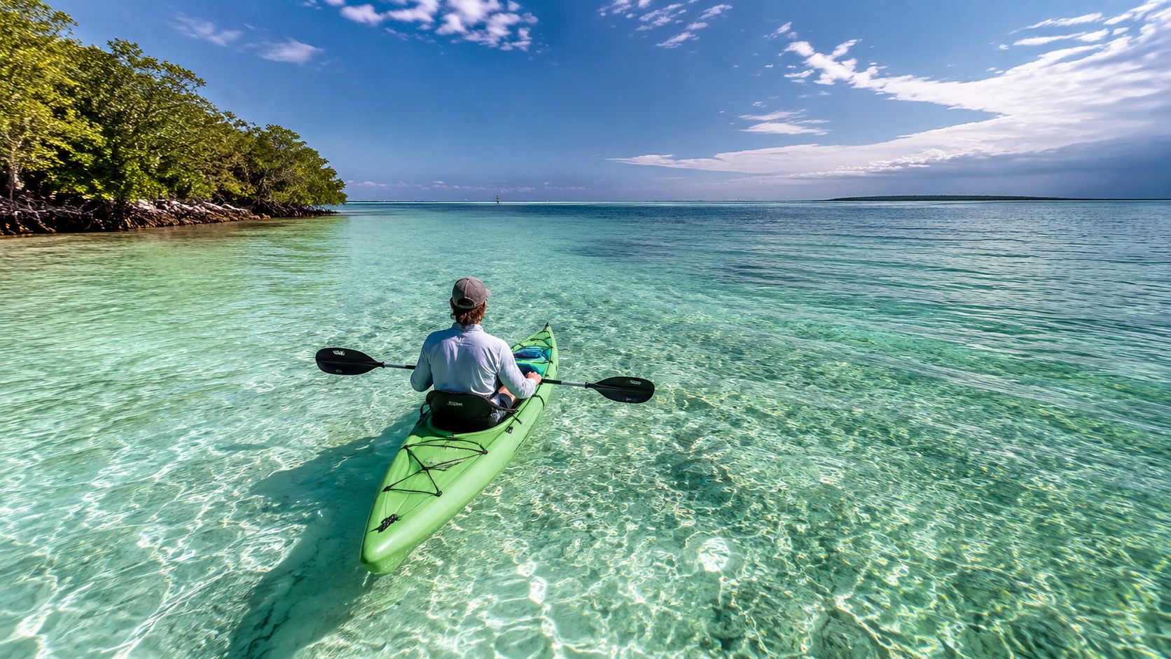 A person paddling in a green kayak through the crystal clear turquoise waters of the Florida Keys.